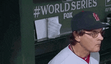 a man wearing a baseball cap and glasses is sitting in a dugout in front of a sign that says world series fox