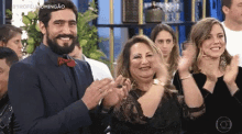 a man in a suit and bow tie is applauding while sitting next to a woman in a black dress .