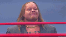 a man with long hair and a gold chain around his neck is standing in a wrestling ring