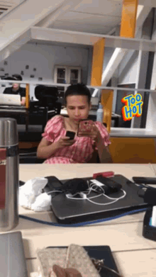 a woman sitting at a desk looking at her phone with a sticker that says too hot on it