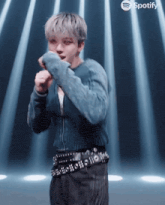 a man in a blue sweater and black pants is dancing in front of spotify