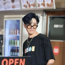 a man wearing glasses is standing in front of an open sign in a restaurant .