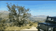 a black land rover is parked on a dirt road with mountains in the background and a tree in the foreground