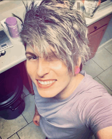 a woman in a purple shirt is smiling in front of a kitchen counter with a purple container on it