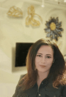 a woman in a black shirt stands in front of a wall with flowers on it