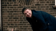 a man in a suit is bending over in front of a brick wall and smiling .