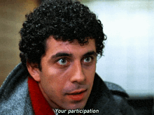 a man with curly hair says " your participation " in front of his face