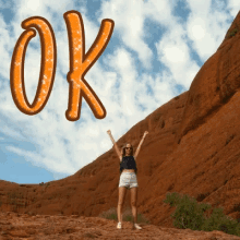 a woman stands on top of a rocky hill with her arms in the air and the word ok above her