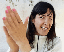 a woman with pink nail polish is smiling and clapping her hands