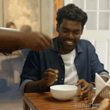 a man sits at a table with a bowl of food in front of a sign that says ' sunio sebi '