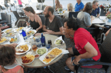 a man in a red shirt that says ' i love you ' sits at a table with other people