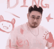 a man wearing glasses and a necklace is standing in front of a wall with drawings and the word leo written on it