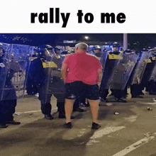 a man in a red shirt is standing in front of a line of police officers with the words rally to me above him