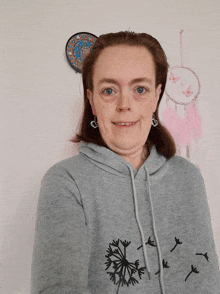 a woman wearing a gray hoodie with a dandelion on it