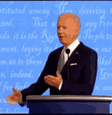 a man in a suit and tie stands at a podium in front of a blue background that says ' that ' on it