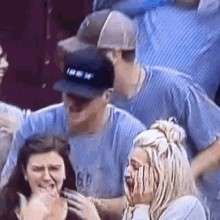 a group of people are sitting in a stadium watching a game . one of the people is wearing a baseball cap .