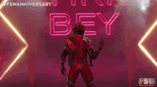 a wrestler in a red outfit is standing in front of a neon sign that says bey