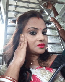 a woman wearing red lipstick and a nose ring holds her hand to her face