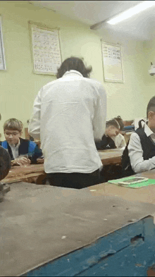 a group of children are sitting at desks in a classroom with a man standing in front of them .