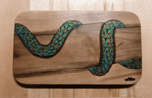 a painting of a snake on a wooden cutting board with the name slender on it