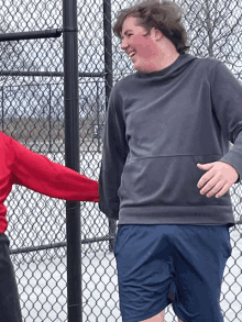 a man in a gray sweatshirt and blue shorts is standing next to a woman in a red shirt