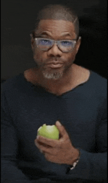 a man with glasses and a beard is holding a green apple .