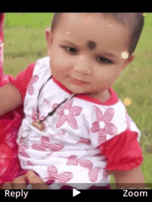 a baby wearing a red and white shirt with flowers on it is being held by a woman in a zoomed in photo