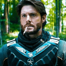 a man with a beard is smoking a cigarette in a forest while wearing a superhero costume .