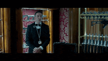 a man in a tuxedo and bow tie says good afternoon mr. wick in front of a display of guns