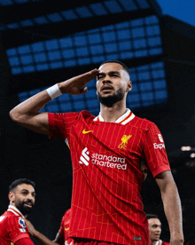 a soccer player wearing a red standard chartered jersey salutes