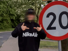 a man wearing a black nike air sweatshirt stands in front of a sign that says 20