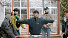 a group of young men are standing in front of a greenhouse and one of them is wearing a jacket with the word navy on it