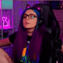 a woman with purple hair and cat ears is sitting in a chair wearing headphones and glasses .