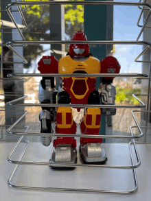 a red and yellow toy robot is behind a metal cage