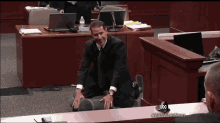 a man in a suit sits on a chair in a courtroom with abc news written on the bottom of the screen