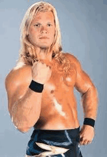 a shirtless wrestler with long blonde hair is standing in front of a blue wall .