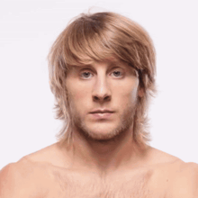 a shirtless man with long blonde hair and a beard is looking at the camera