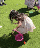 a little girl is picking up easter eggs from the grass .