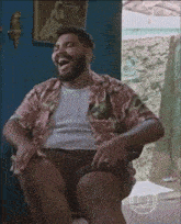 a man with a beard is sitting in a chair with his legs crossed and laughing