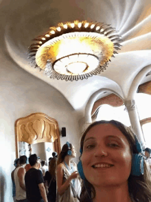 a woman wearing blue headphones smiles in front of a large chandelier