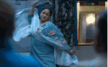 a woman in a blue floral dress is dancing in front of a window