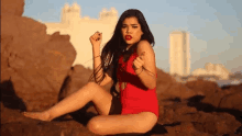 a woman in a red swimsuit is sitting on some rocks on the beach .