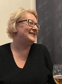 a woman wearing glasses and a necklace with the letter j on it smiles