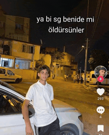 a young man in a white shirt is standing next to a white car in a street at night .