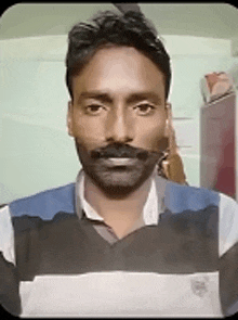 a man with a beard and mustache is wearing a striped shirt and smiling for the camera .