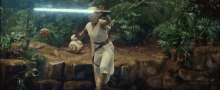 a woman is holding a light saber in a jungle while standing on a rock .