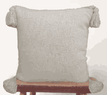 a white pillow with tassels on it is sitting on a wooden stool .