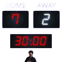 a man stands in front of a scoreboard that says home 7 away 2 and 15:00