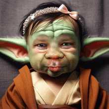 a baby dressed as yoda with a pink bow in her hair