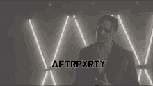 a man in a suit and pearls stands in front of neon lights with the words afterpxrty written on the bottom